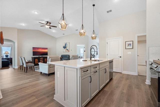 kitchen featuring dark wood-type flooring, sink, appliances with stainless steel finishes, pendant lighting, and a kitchen island with sink