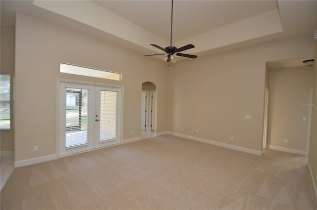 spare room with french doors, ceiling fan, a tray ceiling, and light carpet