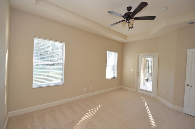 empty room featuring light carpet, ceiling fan, and a tray ceiling