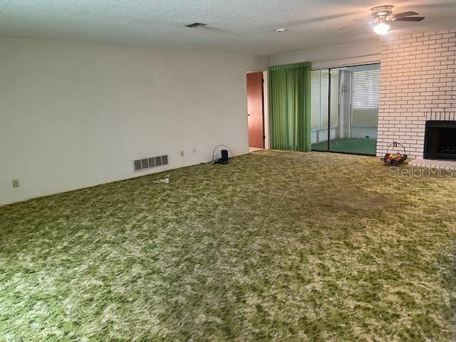 unfurnished living room featuring ceiling fan, carpet flooring, a fireplace, and a textured ceiling