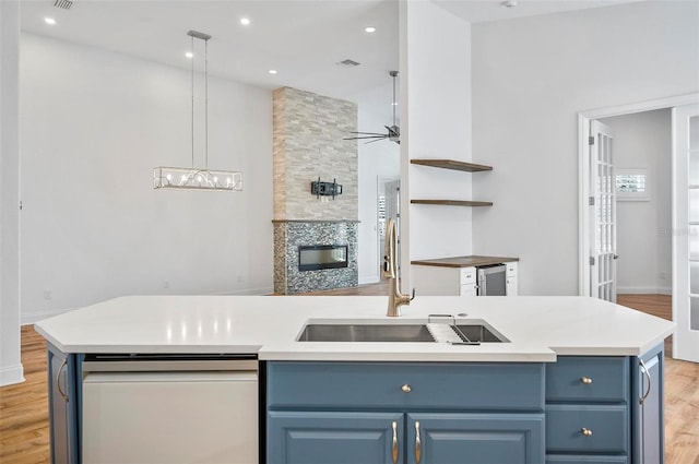 kitchen featuring dishwashing machine, sink, blue cabinets, light hardwood / wood-style floors, and a kitchen island