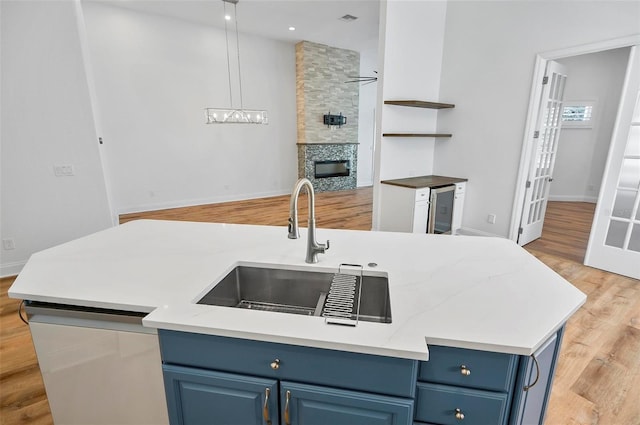 kitchen with blue cabinets, sink, decorative light fixtures, a fireplace, and light hardwood / wood-style floors