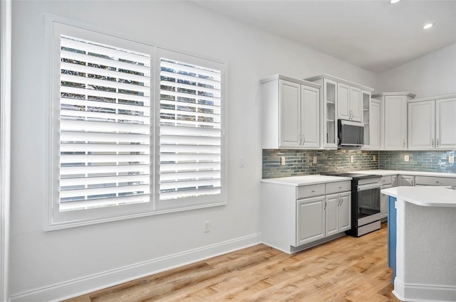 kitchen with decorative backsplash, stainless steel appliances, white cabinets, and light wood-type flooring