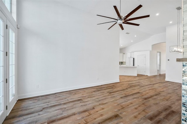 unfurnished living room featuring ceiling fan with notable chandelier, high vaulted ceiling, and hardwood / wood-style floors