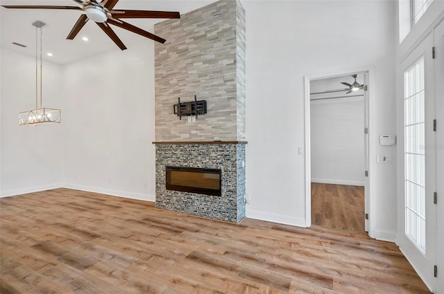 unfurnished living room featuring ceiling fan, light hardwood / wood-style floors, a tile fireplace, and a high ceiling