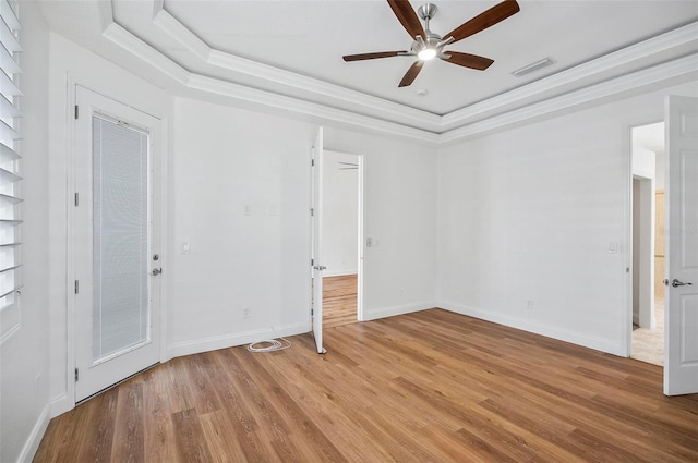 empty room with ornamental molding, light hardwood / wood-style floors, a raised ceiling, and ceiling fan