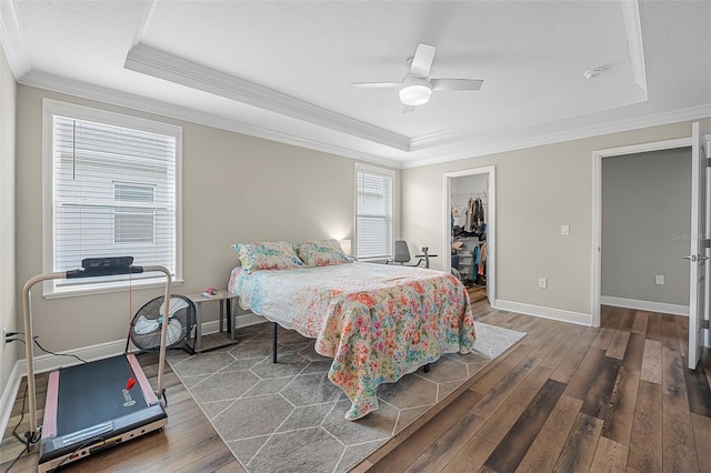 bedroom featuring crown molding, a walk in closet, dark hardwood / wood-style floors, and a tray ceiling