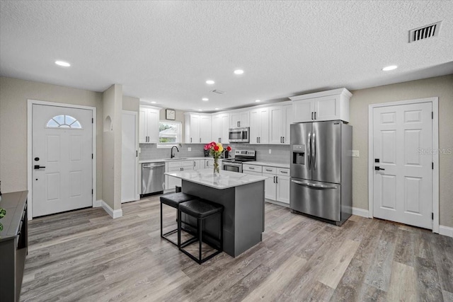 kitchen featuring a kitchen island, stainless steel appliances, white cabinets, a kitchen bar, and light wood-type flooring