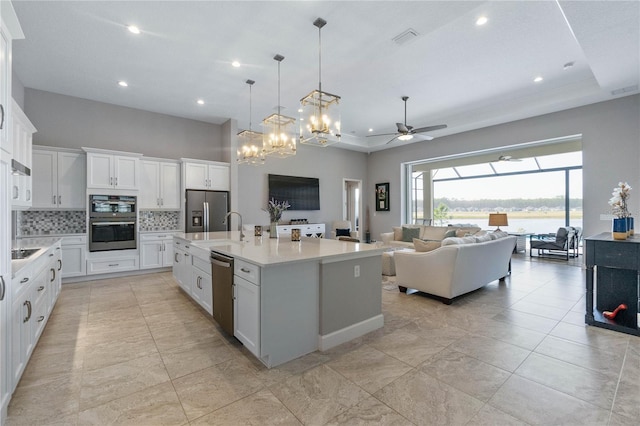 kitchen featuring white cabinets, backsplash, stainless steel fridge with ice dispenser, a raised ceiling, and a center island with sink