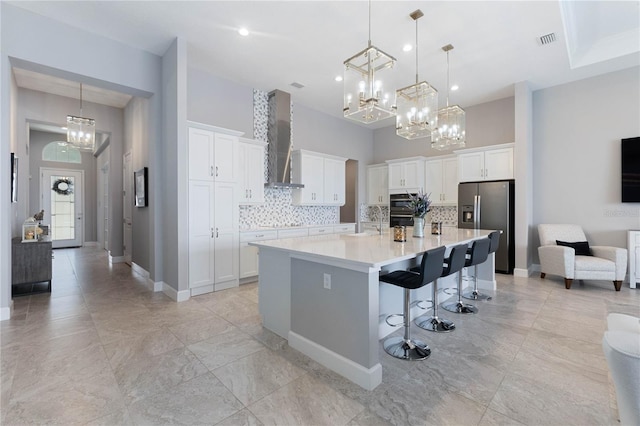 kitchen with stainless steel fridge, white cabinets, a kitchen bar, a large island with sink, and wall chimney range hood