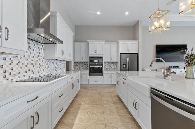 kitchen featuring decorative light fixtures, white cabinetry, light stone counters, stainless steel appliances, and wall chimney exhaust hood