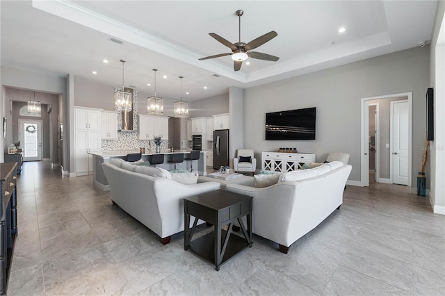 living room with a tray ceiling, ceiling fan with notable chandelier, and a high ceiling