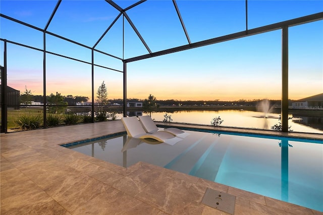 pool at dusk with a patio, glass enclosure, and a water view