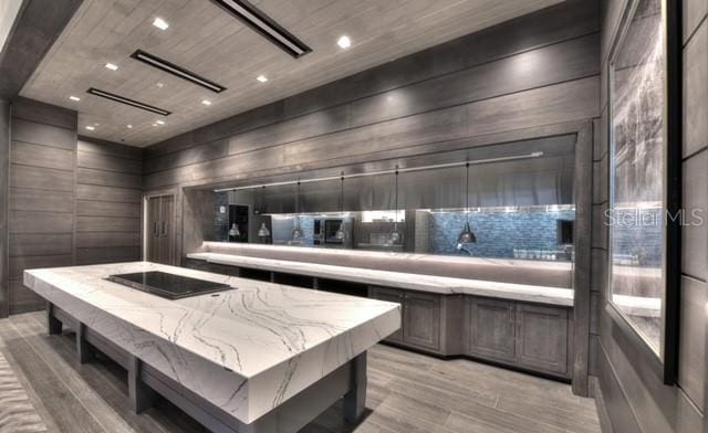 kitchen with wood walls, a large island, light stone countertops, and light wood-type flooring