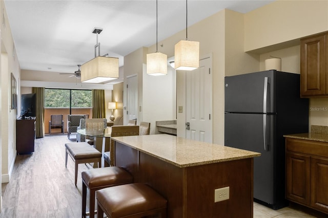 kitchen with a breakfast bar area, light stone counters, refrigerator, a kitchen island, and pendant lighting