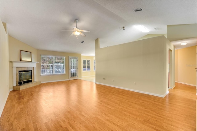 unfurnished living room featuring a tiled fireplace, lofted ceiling, light hardwood / wood-style floors, and ceiling fan