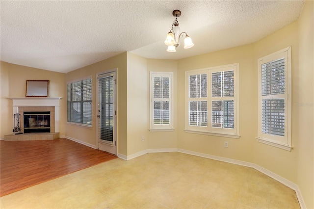 unfurnished living room featuring a chandelier, a tiled fireplace, a textured ceiling, and light wood-type flooring