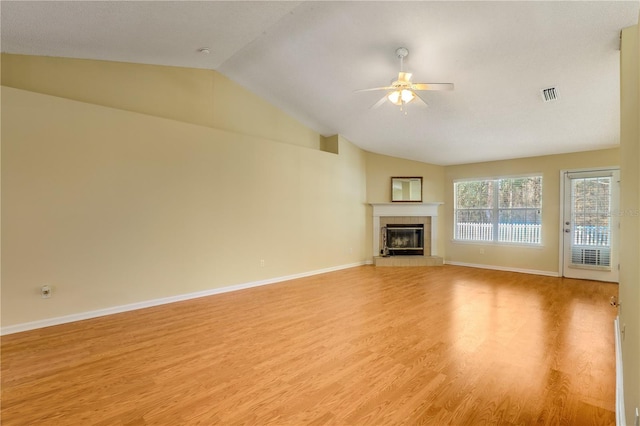 unfurnished living room featuring ceiling fan, lofted ceiling, a tiled fireplace, and light wood-type flooring