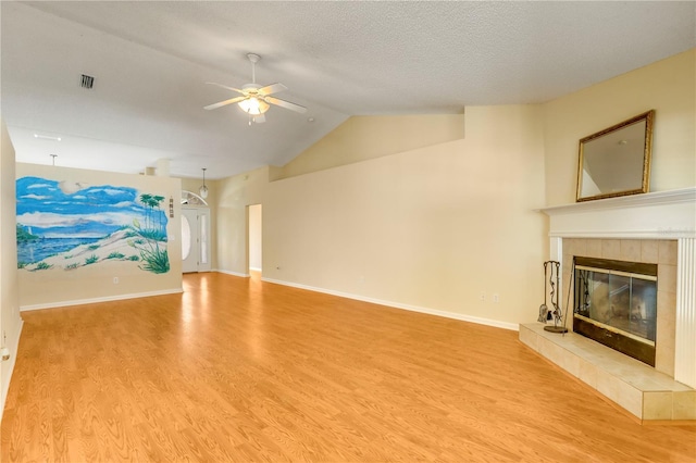 unfurnished living room with a tile fireplace, ceiling fan, hardwood / wood-style floors, a textured ceiling, and vaulted ceiling