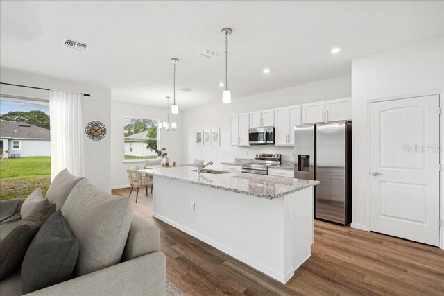 kitchen with white cabinetry, decorative light fixtures, appliances with stainless steel finishes, an island with sink, and light stone countertops