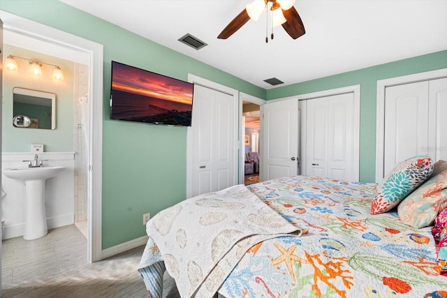 bedroom featuring two closets, ensuite bath, and ceiling fan