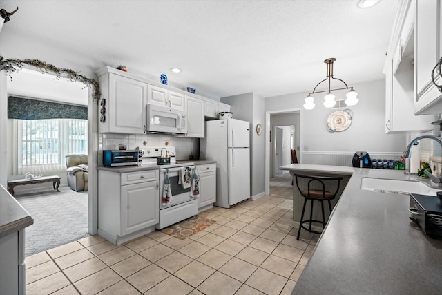 kitchen with decorative light fixtures, white cabinetry, sink, backsplash, and white appliances