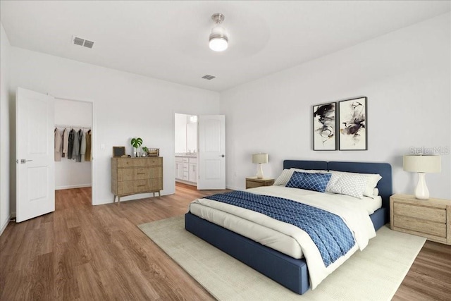 bedroom with a walk in closet, connected bathroom, hardwood / wood-style floors, and a closet