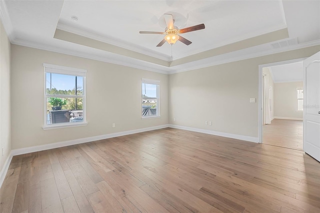 empty room with light hardwood / wood-style flooring, ornamental molding, a raised ceiling, and a healthy amount of sunlight