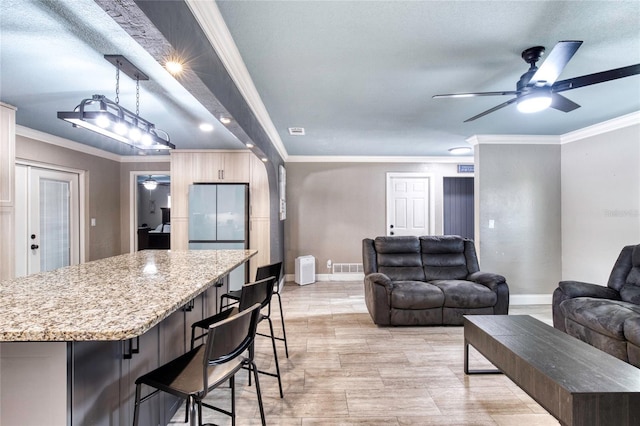 kitchen featuring a kitchen island, open floor plan, light stone countertops, decorative light fixtures, and crown molding