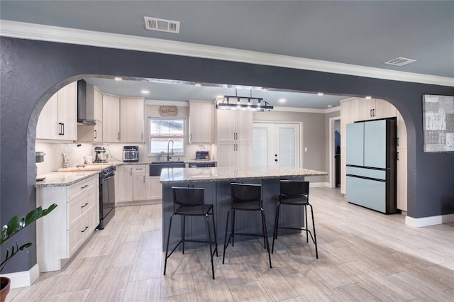 kitchen with arched walkways, visible vents, black electric range, freestanding refrigerator, and a center island