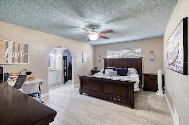 bedroom featuring arched walkways, a textured wall, a textured ceiling, ceiling fan, and baseboards