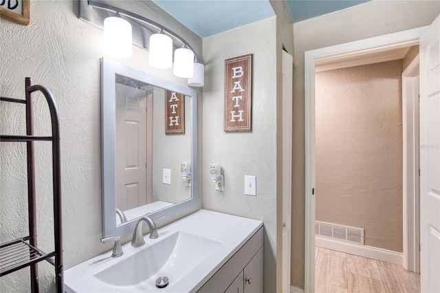 bathroom featuring a textured wall, wood finished floors, vanity, visible vents, and baseboards