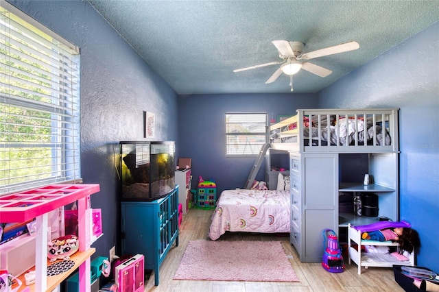 bedroom featuring light wood finished floors, a ceiling fan, a textured ceiling, and a textured wall