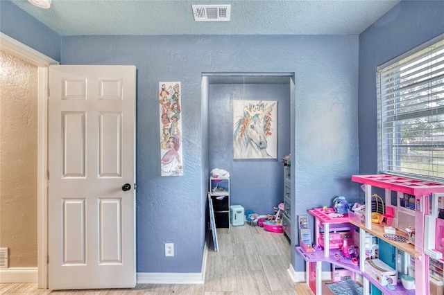 game room with visible vents, a textured wall, and wood finished floors