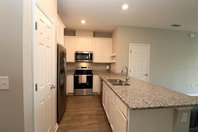 kitchen featuring sink, white cabinetry, kitchen peninsula, stainless steel appliances, and light stone countertops