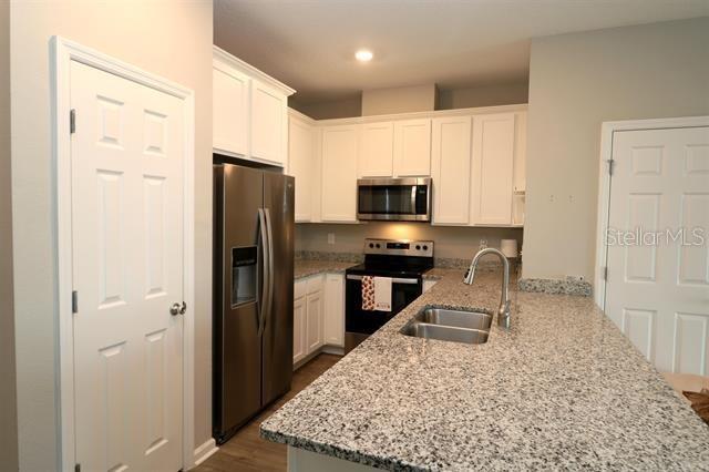 kitchen featuring sink, stainless steel appliances, light stone countertops, white cabinets, and kitchen peninsula