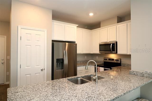 kitchen featuring stainless steel appliances, white cabinetry, sink, and kitchen peninsula