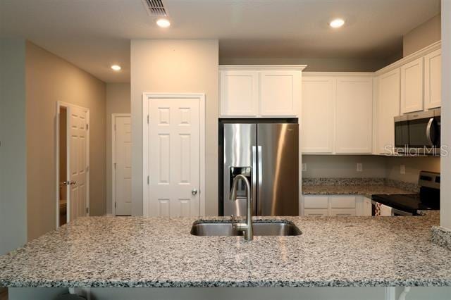 kitchen with white cabinetry, appliances with stainless steel finishes, light stone countertops, and sink