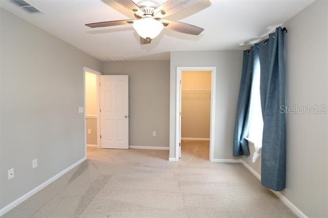 unfurnished bedroom featuring ceiling fan, a walk in closet, light carpet, and a closet