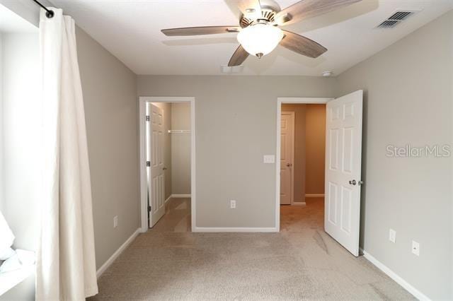 unfurnished bedroom featuring a spacious closet, light colored carpet, a closet, and ceiling fan