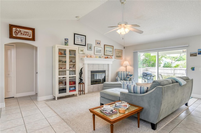 living room with a tile fireplace, light tile patterned flooring, lofted ceiling, and ceiling fan