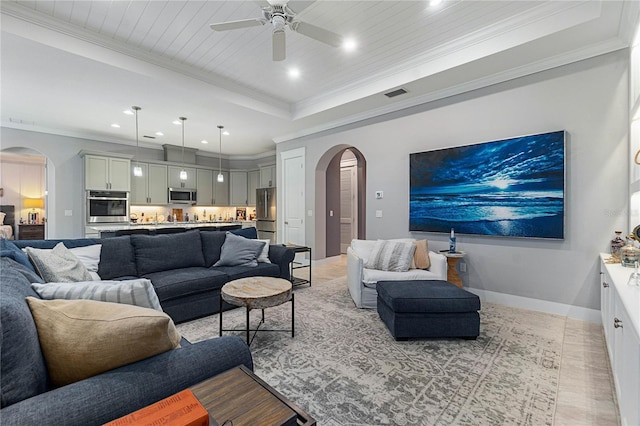 living area with visible vents, baseboards, arched walkways, crown molding, and a raised ceiling