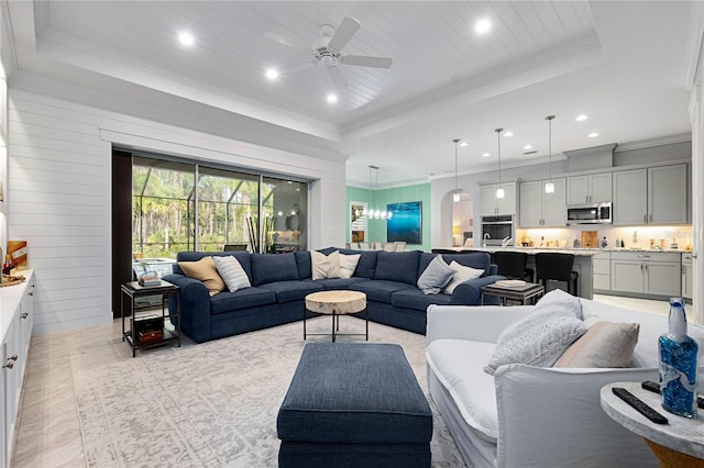 living area with wood ceiling, a ceiling fan, a tray ceiling, and ornamental molding