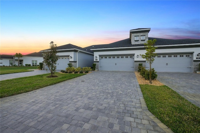 view of front of property featuring a garage, decorative driveway, a lawn, and stucco siding