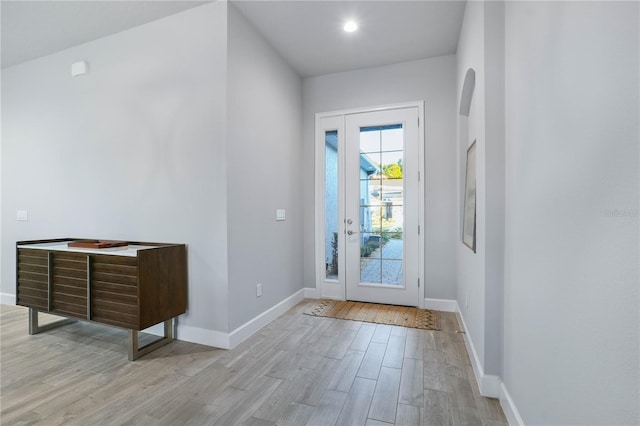 doorway featuring arched walkways, light wood-style flooring, and baseboards