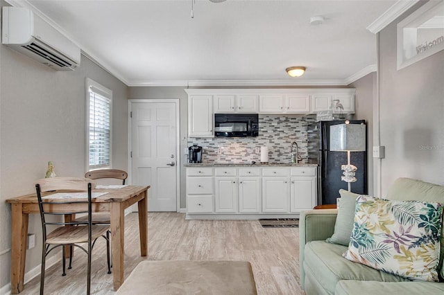 kitchen with white cabinetry, a wall mounted AC, ornamental molding, light hardwood / wood-style floors, and black appliances