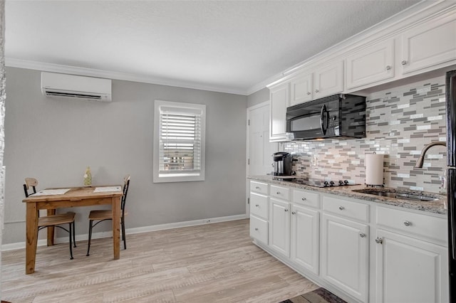 kitchen featuring sink, white cabinetry, a wall unit AC, light hardwood / wood-style floors, and black appliances