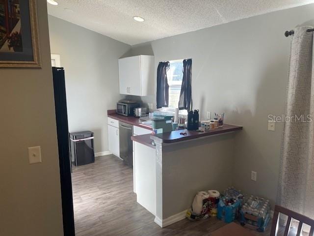 kitchen with appliances with stainless steel finishes, dark hardwood / wood-style floors, a textured ceiling, white cabinets, and kitchen peninsula