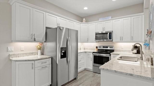 kitchen with sink, white cabinets, light stone counters, stainless steel appliances, and light wood-type flooring