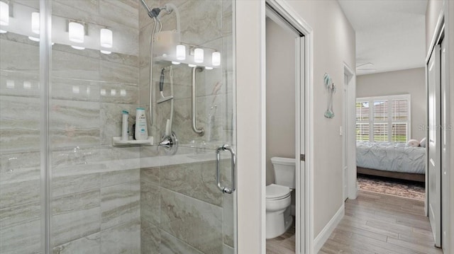 bathroom with hardwood / wood-style flooring, a shower with shower door, and toilet